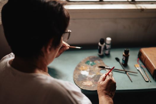A focused adult artist painting with tools and palette in an indoor studio setting.