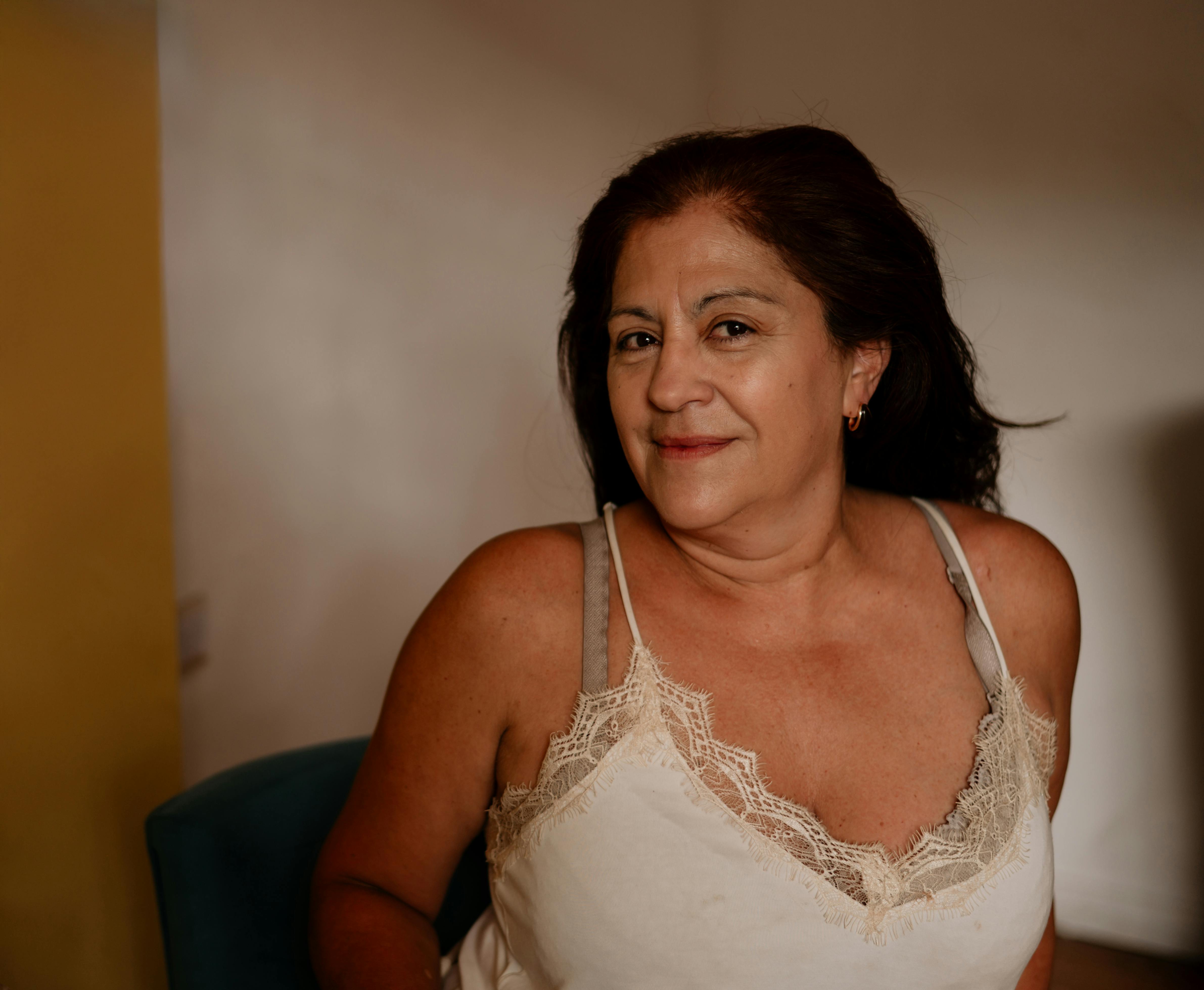 Zadarmo Priateľská žena v čipkovanom tope, sediaca vnútri s vrúcnym úsmevom. Fotka z fotobanky