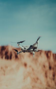 A drone captured mid-flight against a striking desert cliff under a blue sky.