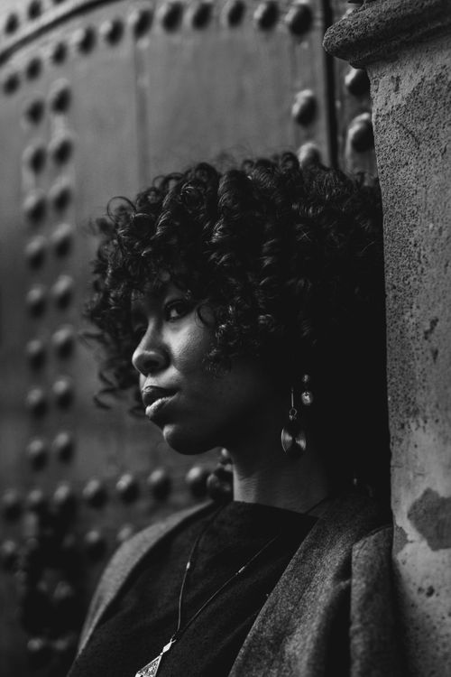 Free Stylish black and white portrait of a young woman with curly hair leaning against a textured wall. Stock Photo