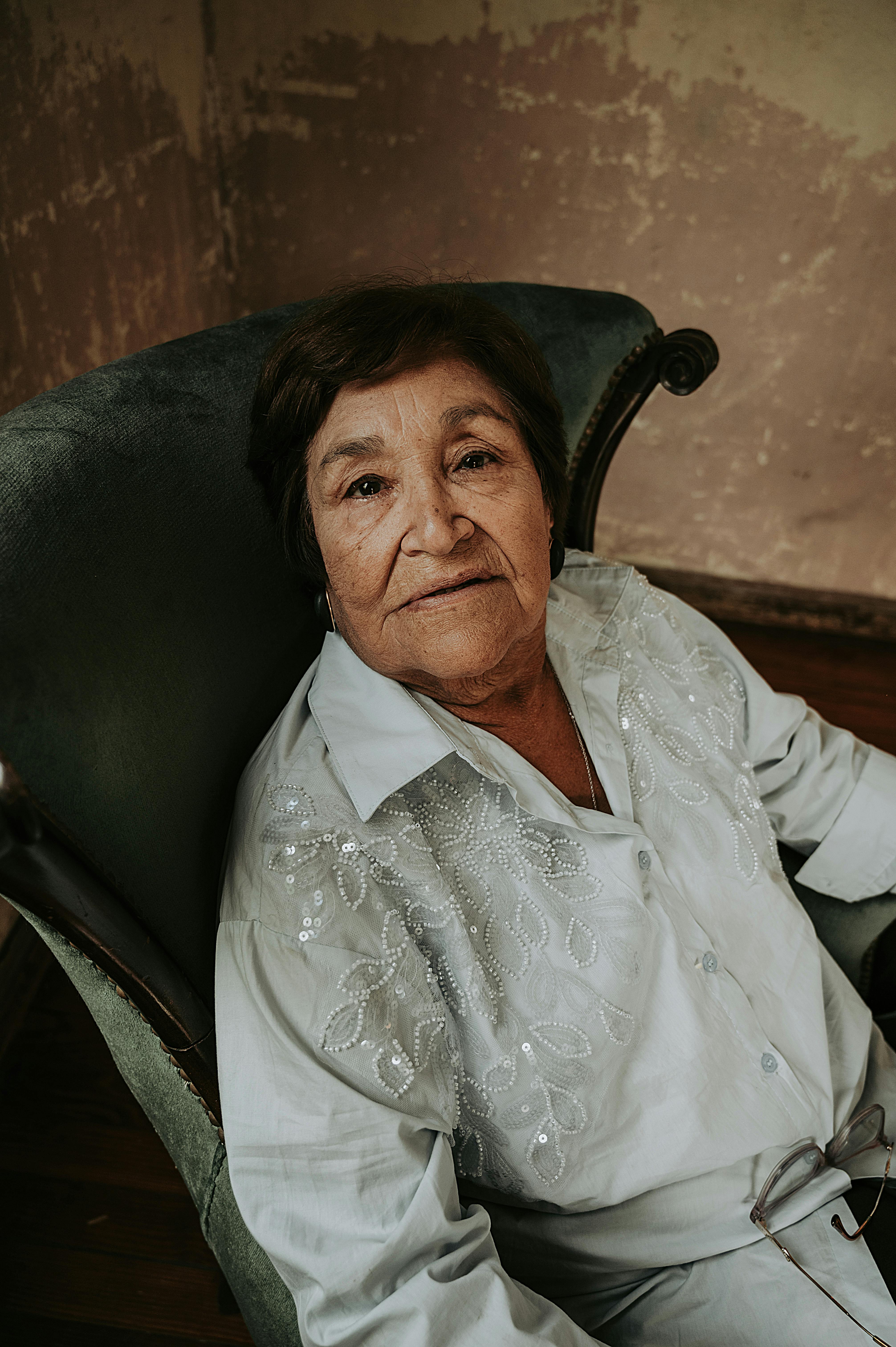 Zadarmo Staršia žena sediaca vo vintage kresle so zamysleným výrazom v interiéri. Fotka z fotobanky