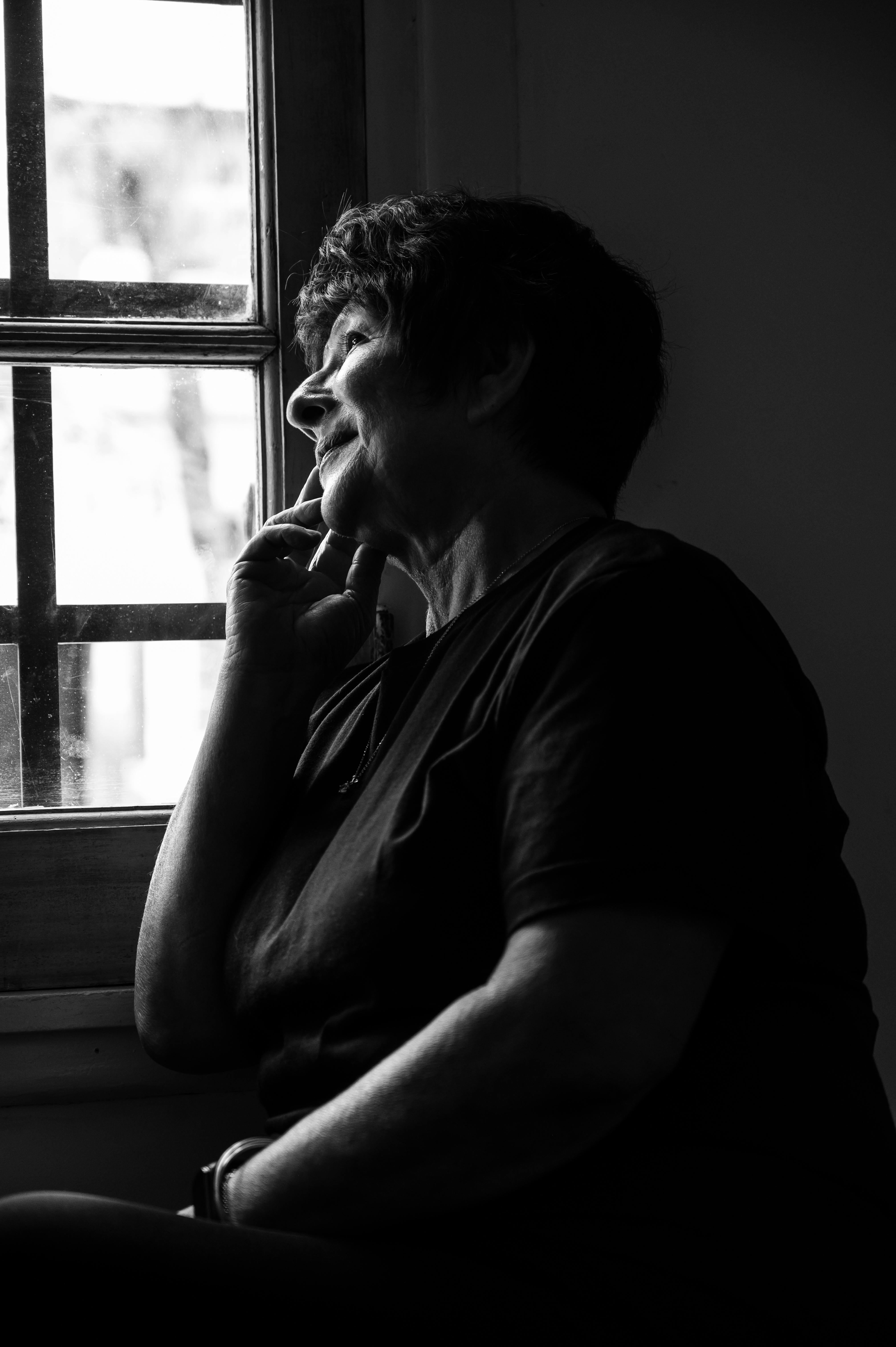Zadarmo Zamyslená staršia žena hľadí z okna, zachytená na melancholickej čiernobielej fotografii. Fotka z fotobanky