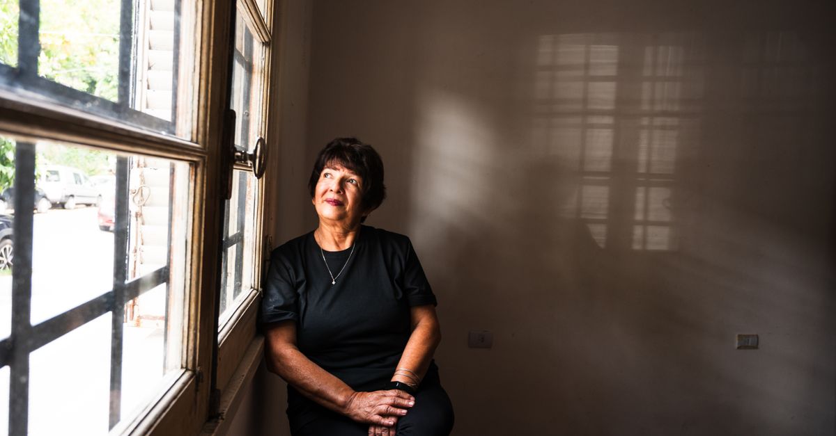 A thoughtful senior woman sitting by a window in a softly lit room, lost in contemplation.