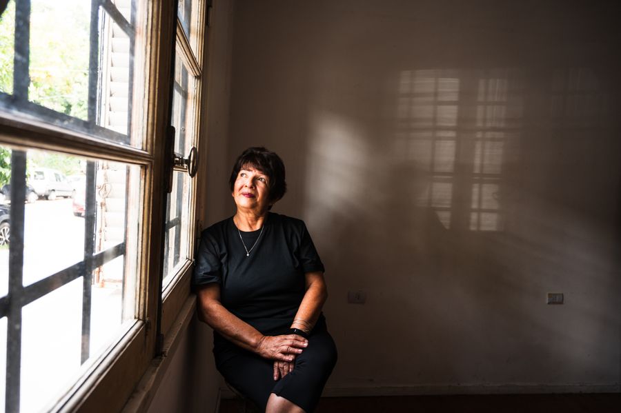 A woman sits by a sunlit window, deep in thought