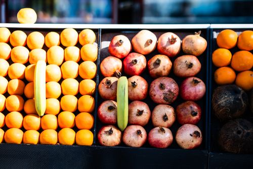 Free Colorful rows of fresh fruits including oranges, pomegranates, and bananas at a market. Stock Photo