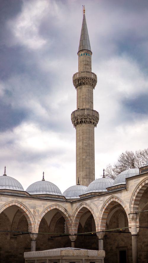 Free A majestic minaret towers above historical arches under a cloudy sky. Stock Photo