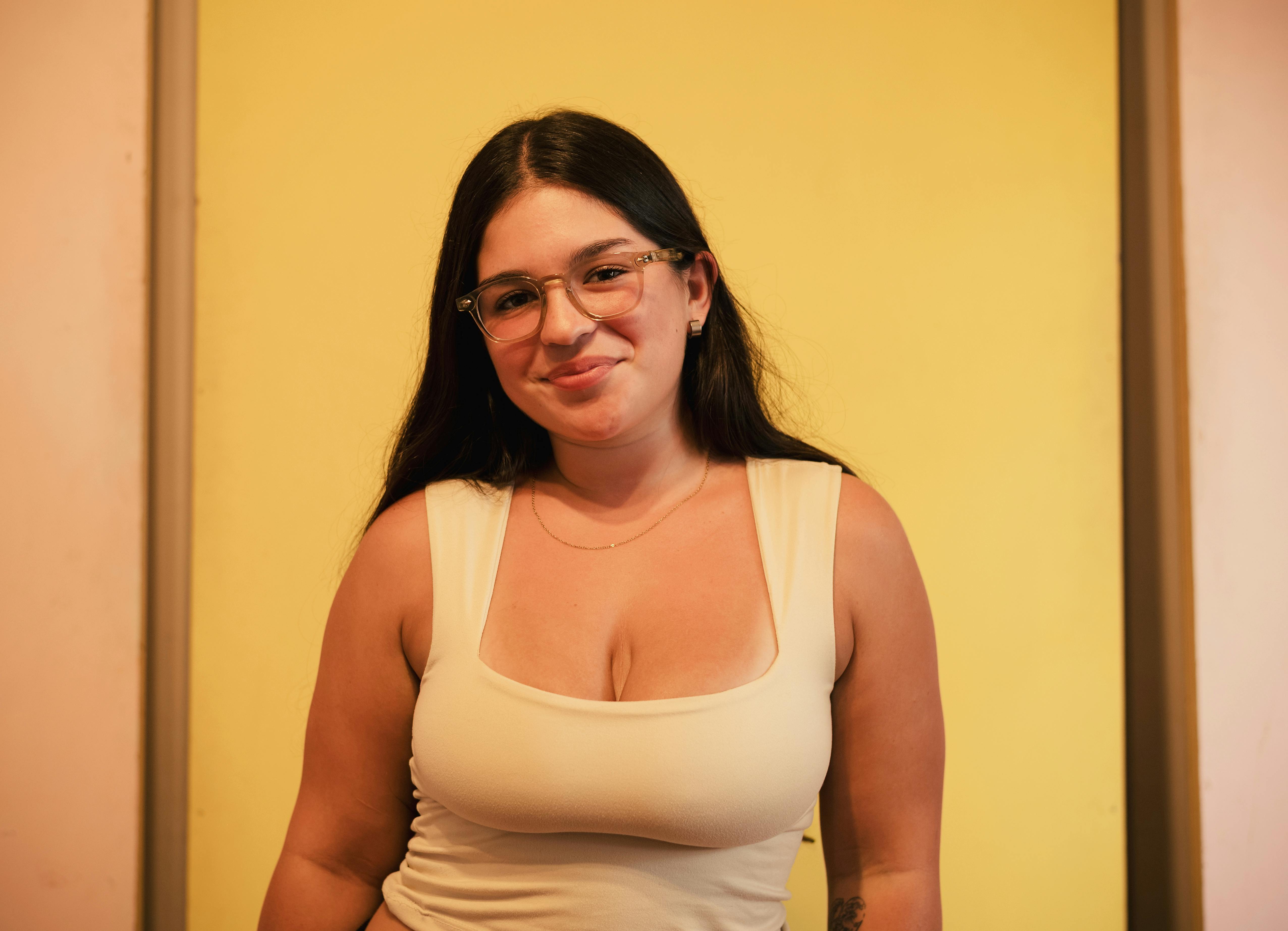 Безкоштовне Усміхнена жінка в окулярах позує на жовтому фоні в приміщенні. стокове фото