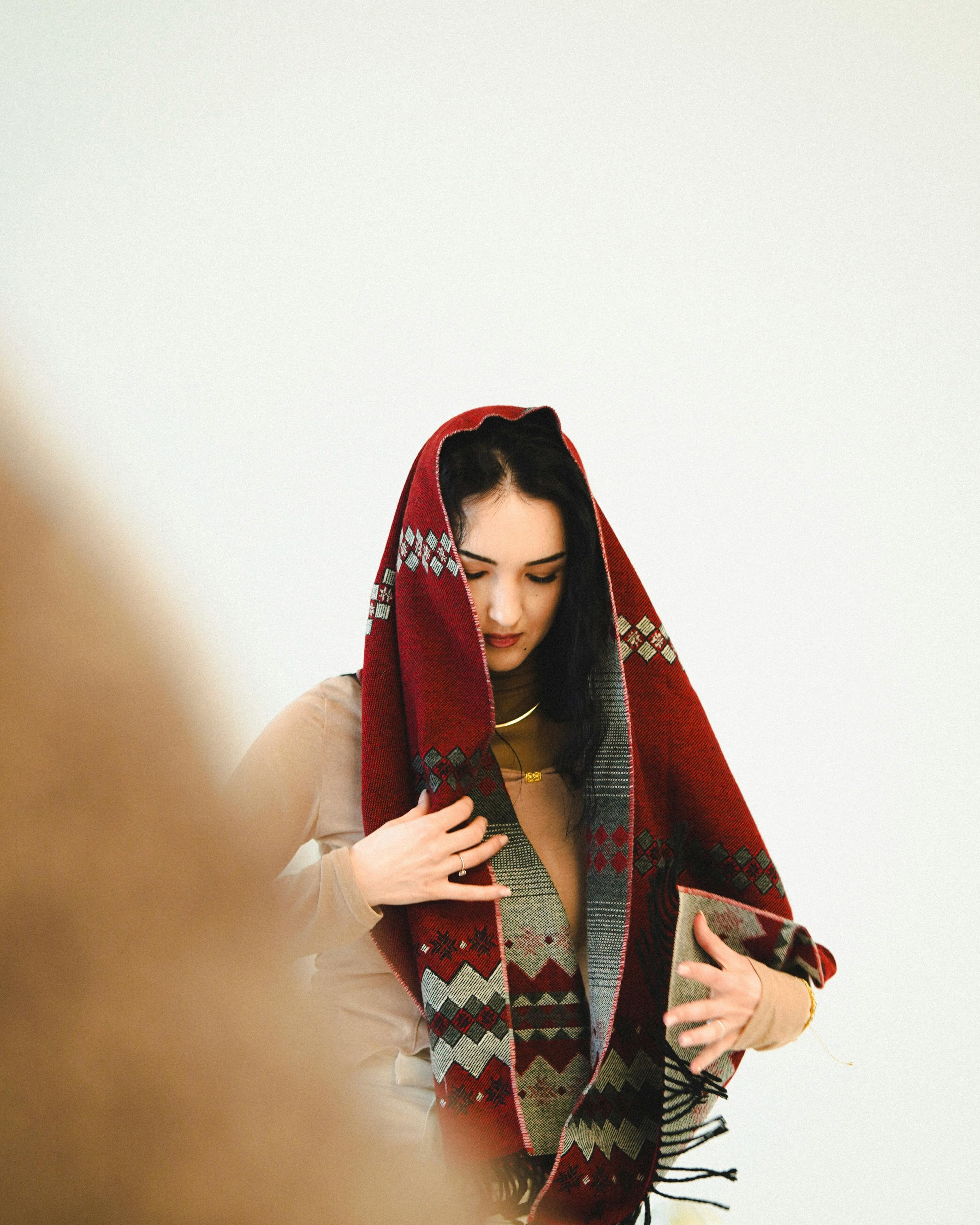 무료 붉은색 기하학적 무늬 숄을 두른 여성이 평온한 자세로 서 있는 모습의 초상화. 스톡 사진