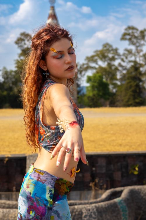 Free Young woman with vibrant style extends hand outdoors on a sunny day. Stock Photo