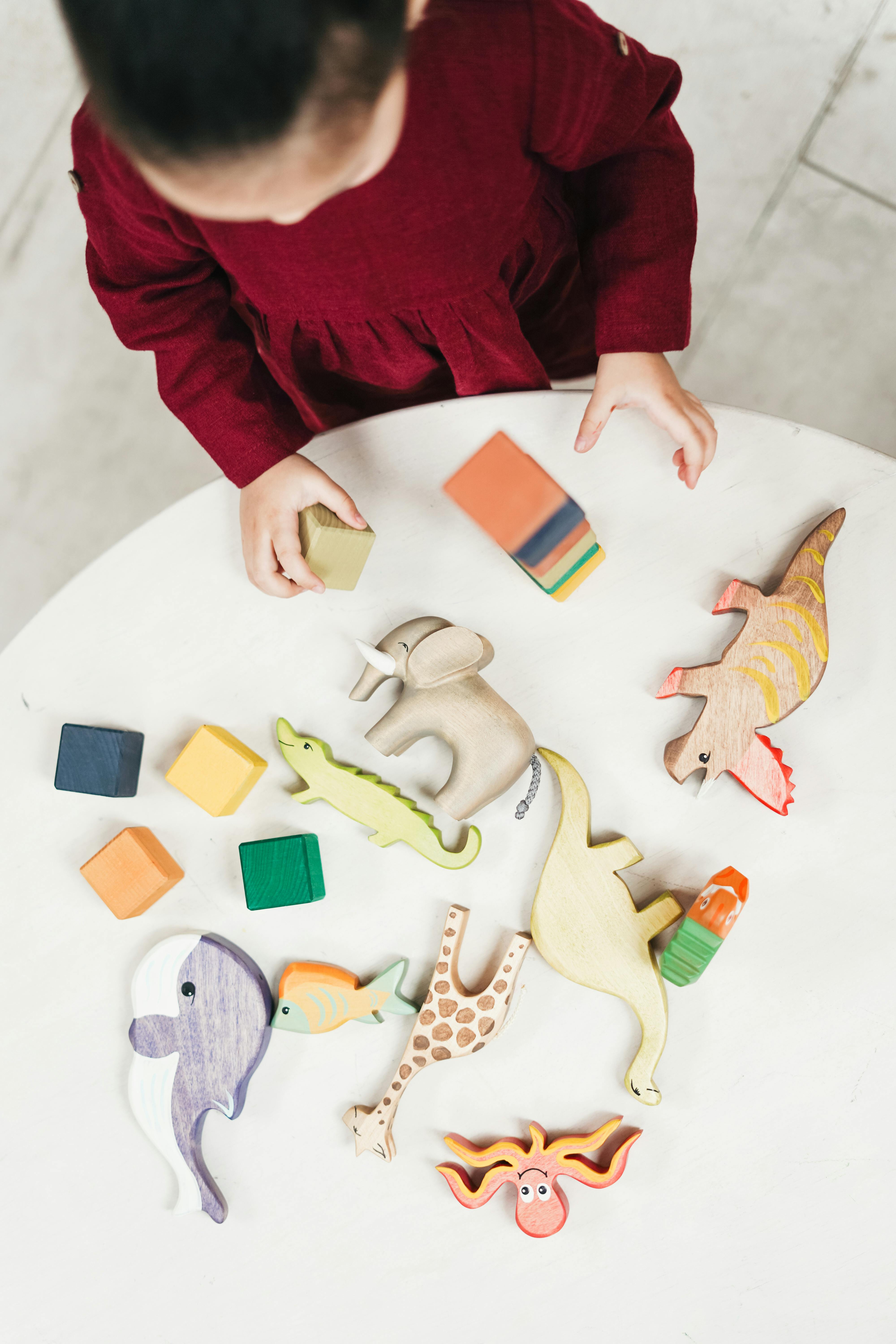 overhead photo of young girl in red dress playing with building blocks and toys