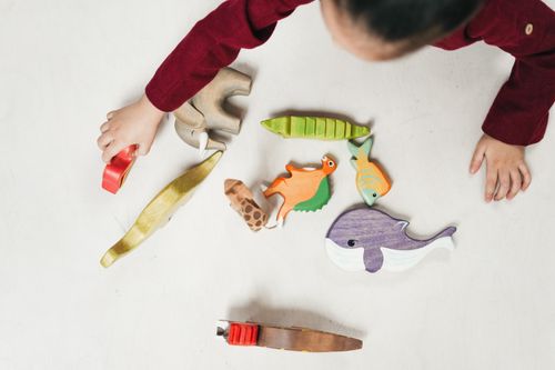 Free Overhead view of a child playing with colorful wooden animal toys on a white table. Stock Photo