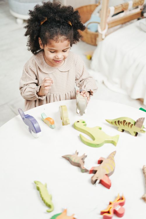 Free Cheerful child engages with colorful wooden dinosaur toys in a bright room. Stock Photo