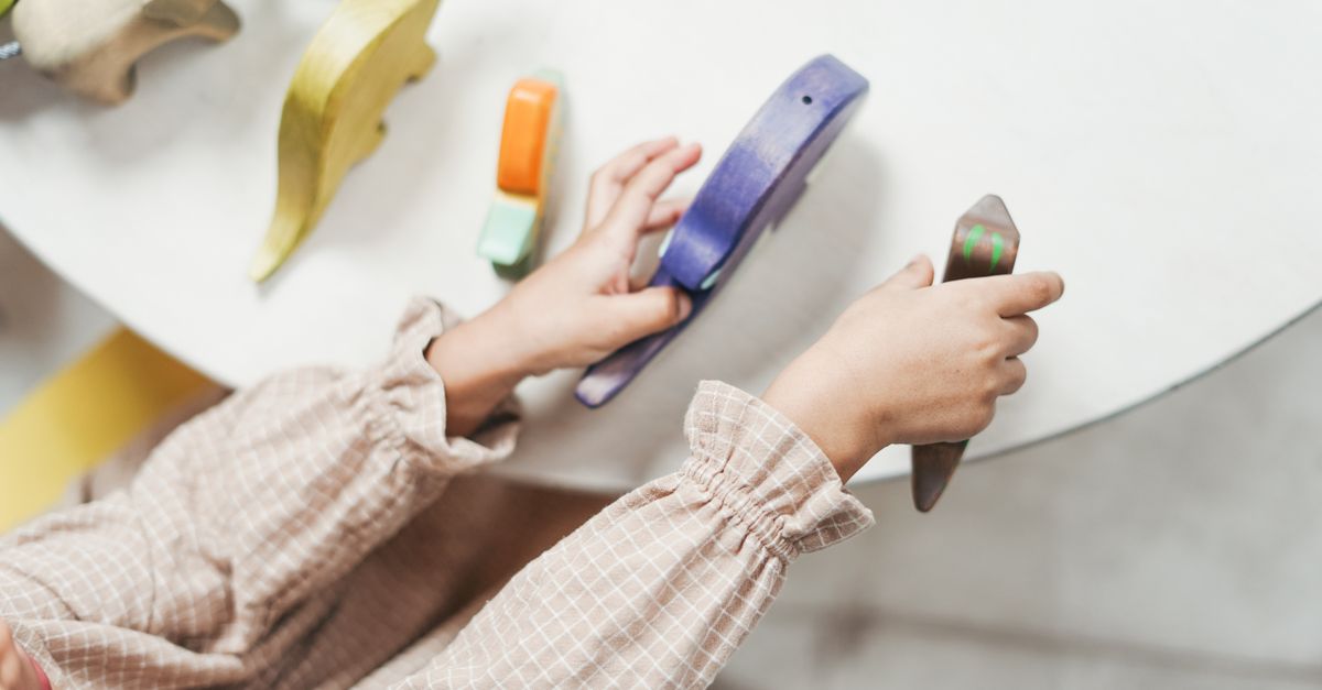 Top view of a child playing with colorful wooden toys, focusing on hands and table.