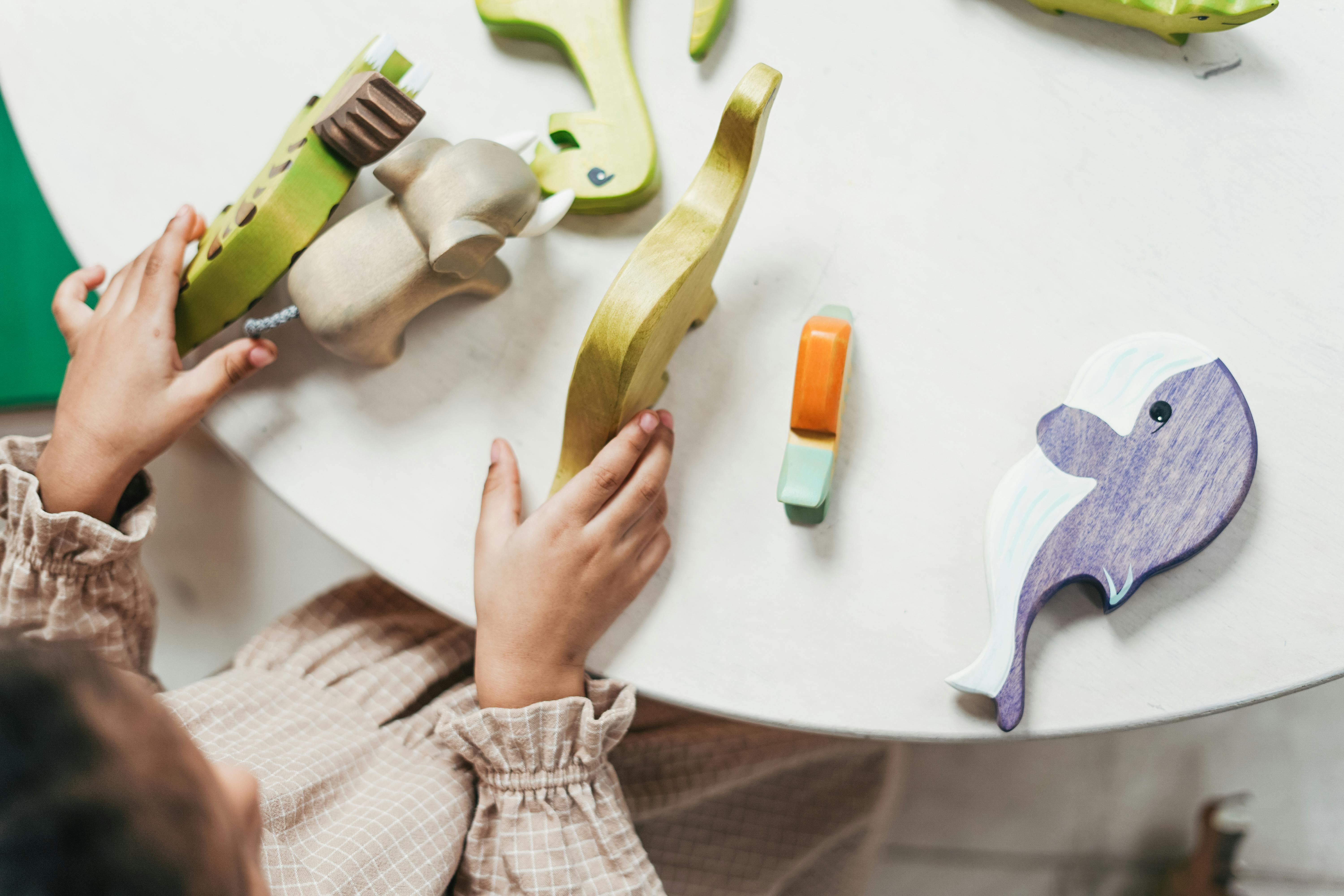 overhead photo of young girl playing with wooden toys on white table