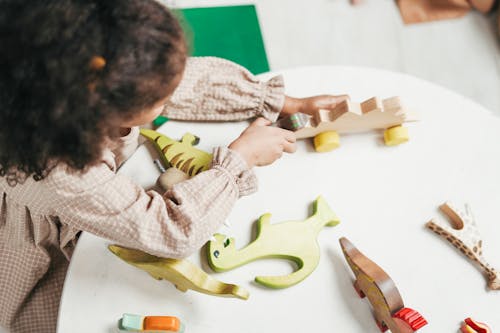 Overhead Photo of Young Girl Playing with Wooden Toys on White Table