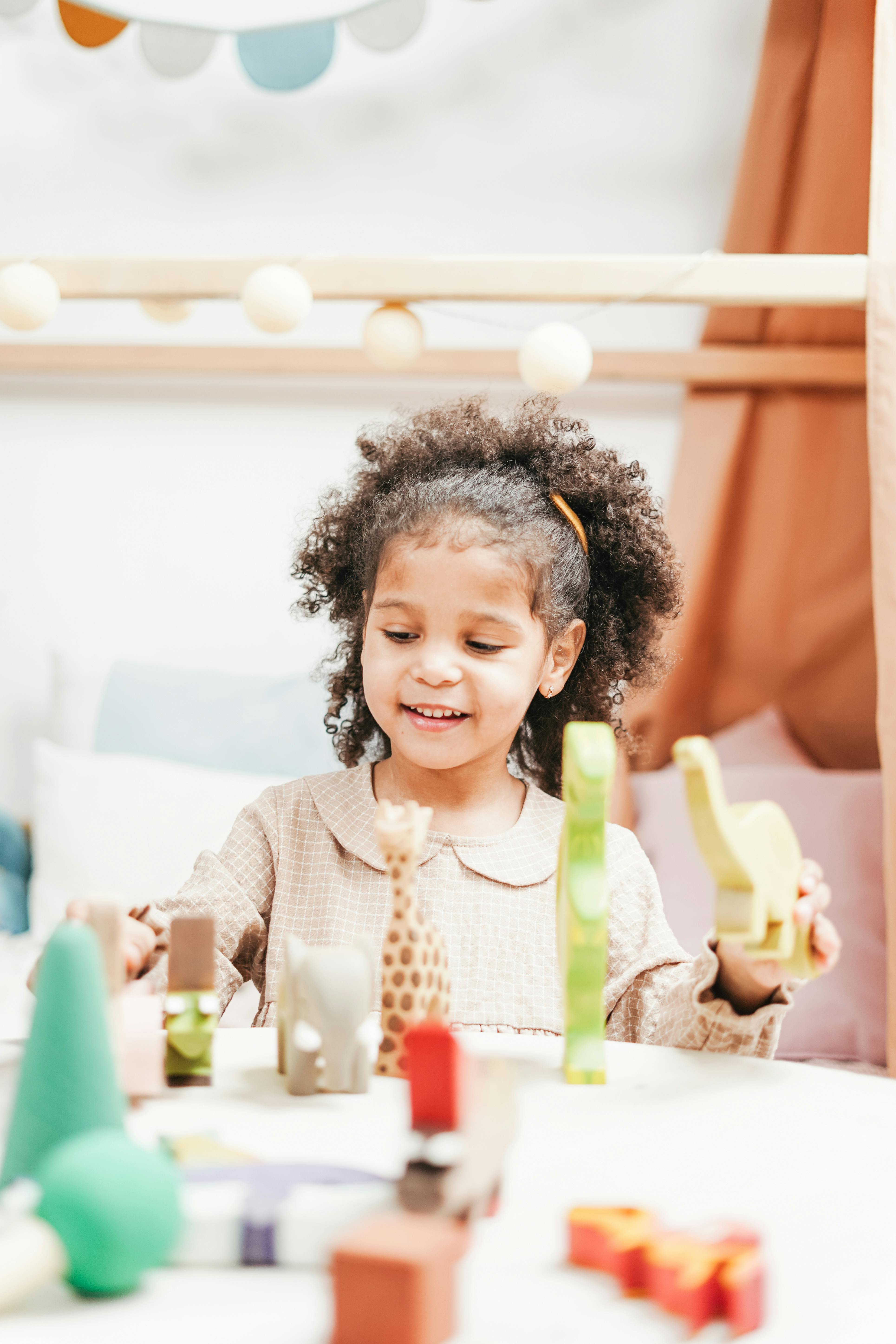 selective focus photo of smiling young girl playing with wooden toys on white table