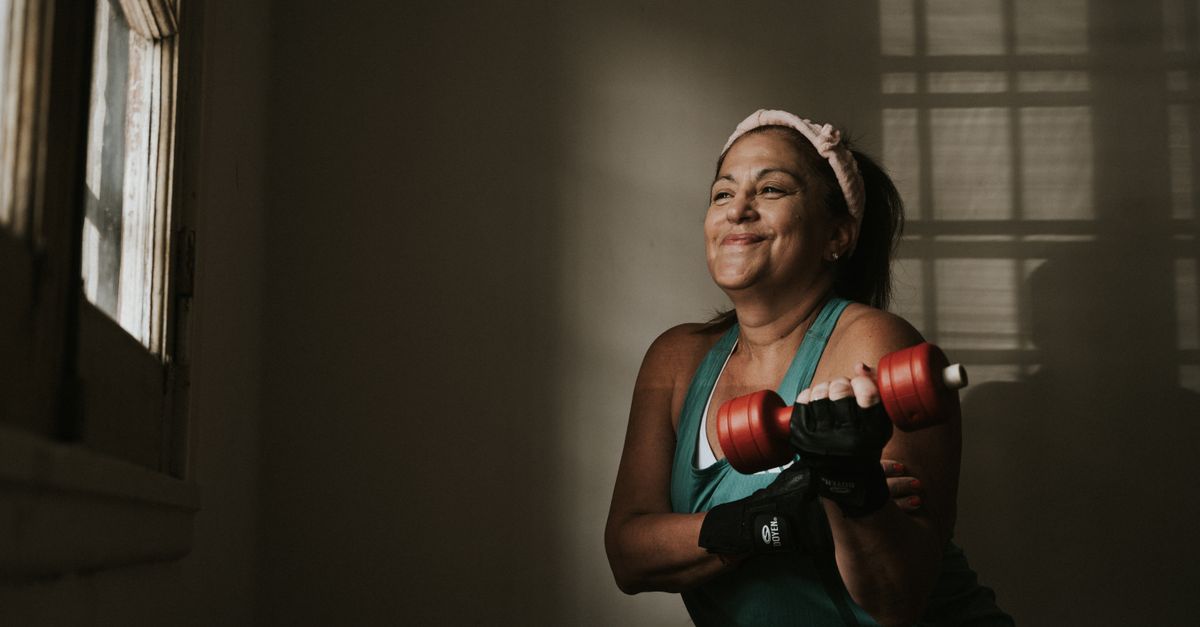 Confident middle-aged woman lifting dumbbells indoors