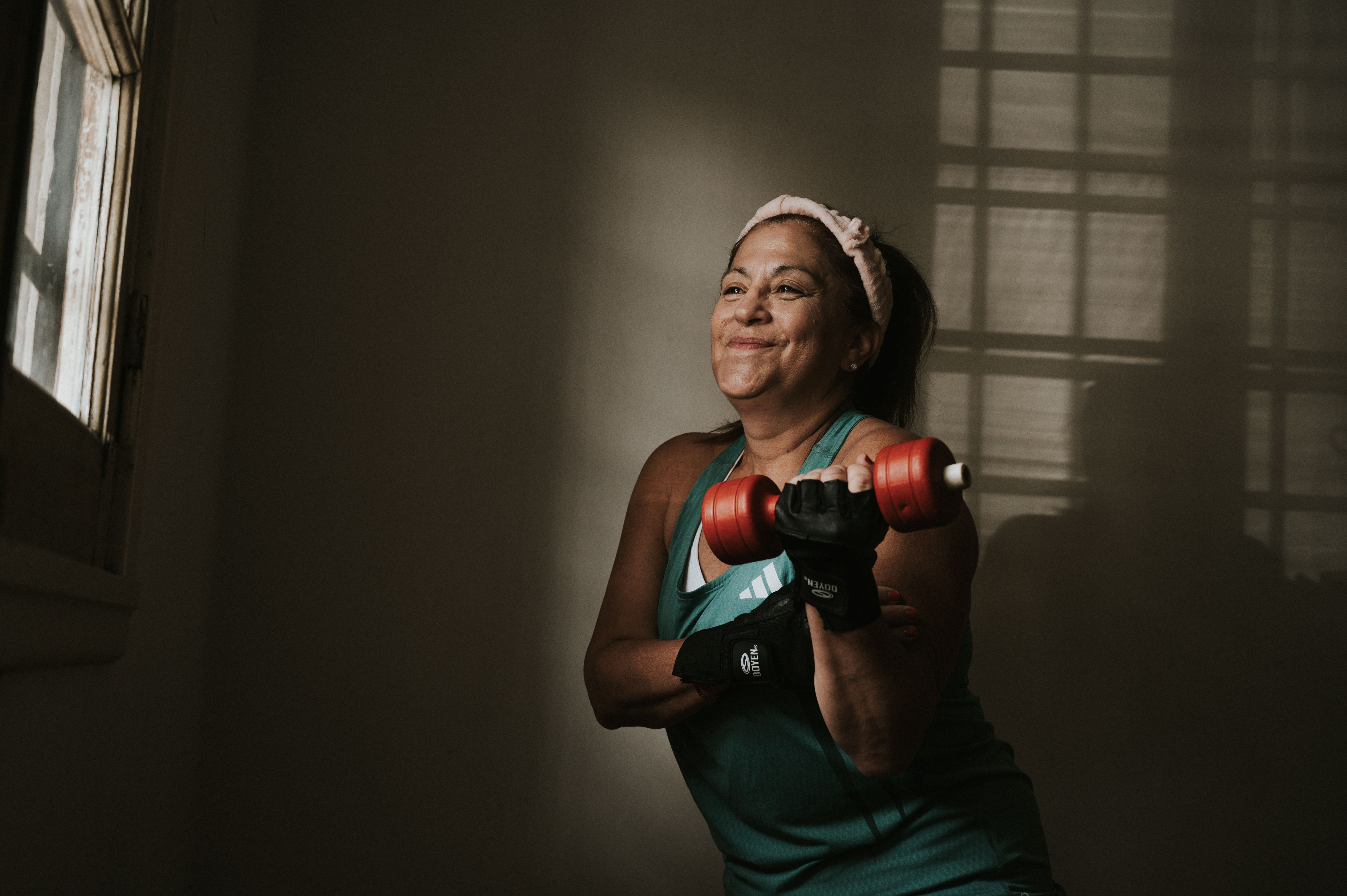Confident middle-aged woman lifting dumbbells indoors, focused on fitness and strength training.