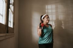 Middle-aged woman in workout attire lifting a dumbbell indoors, promoting fitness and healthy lifestyle.