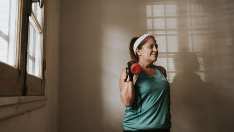 Middle-aged woman in workout attire lifting a dumbbell indoors, promoting fitness and healthy lifestyle.