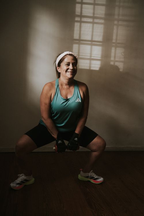 Free Middle-aged woman in activewear performing a squat exercise with weights indoors. Stock Photo