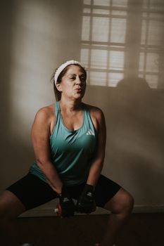 A middle-aged woman working out with dumbbells in a well-lit indoor setting, emphasizing fitness and strength.
