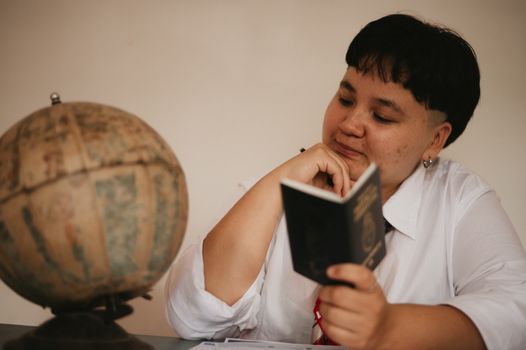 A pensive young adult reading a passport next to a vintage globe, symbolizing travel dreams.