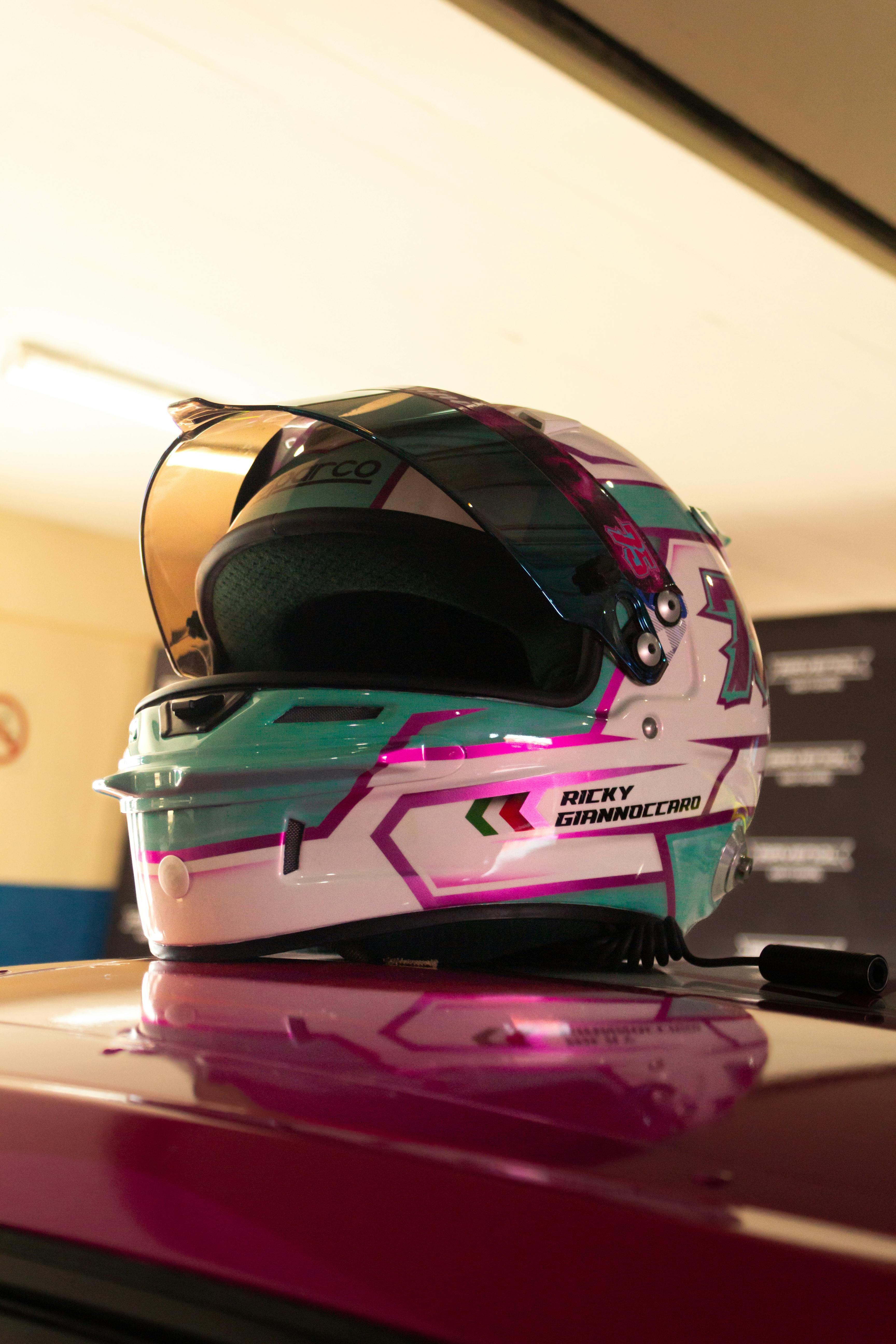 Vibrant racing helmet sits on car roof in indoor garage with warm lighting.