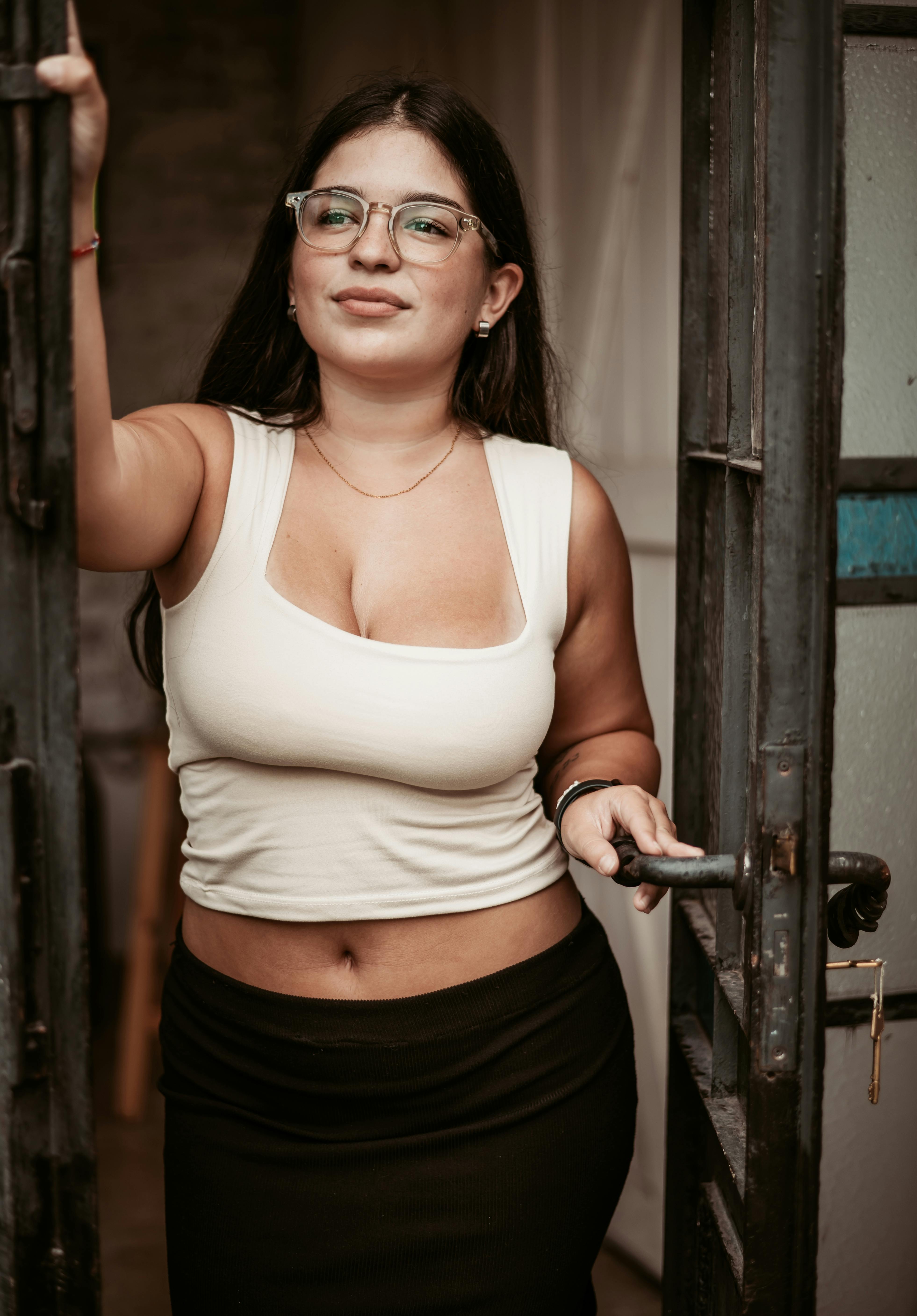 Безкоштовне Жінка у білому топі та чорній спідниці впевнено відчиняє двері, випромінюючи невимушену елегантність. стокове фото