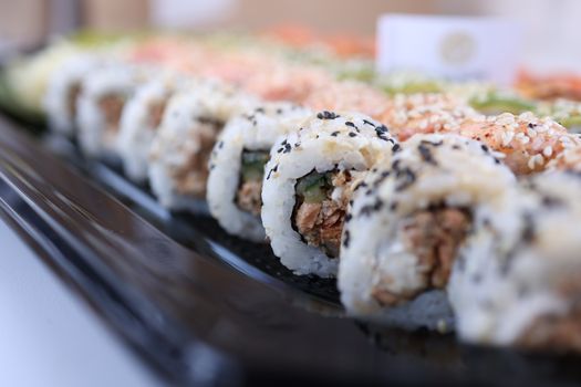 Close-up of assorted sushi rolls on a black tray, showcasing detailed textures and colors.