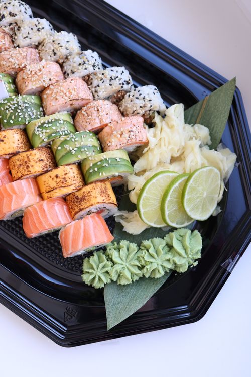 Free A delicious assortment of sushi rolls with lime, wasabi, and ginger garnishes in a black serving tray. Stock Photo