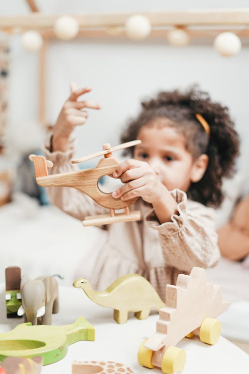 Girl in White Long Sleeve Dress Holding Brown Wooden Helicopter