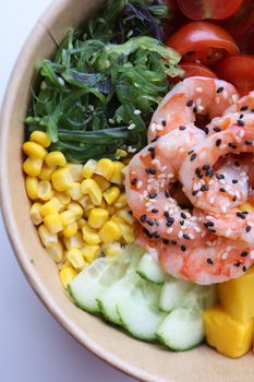 Vibrant poke bowl with shrimp, seaweed, corn, cucumber, tomatoes, and mango.