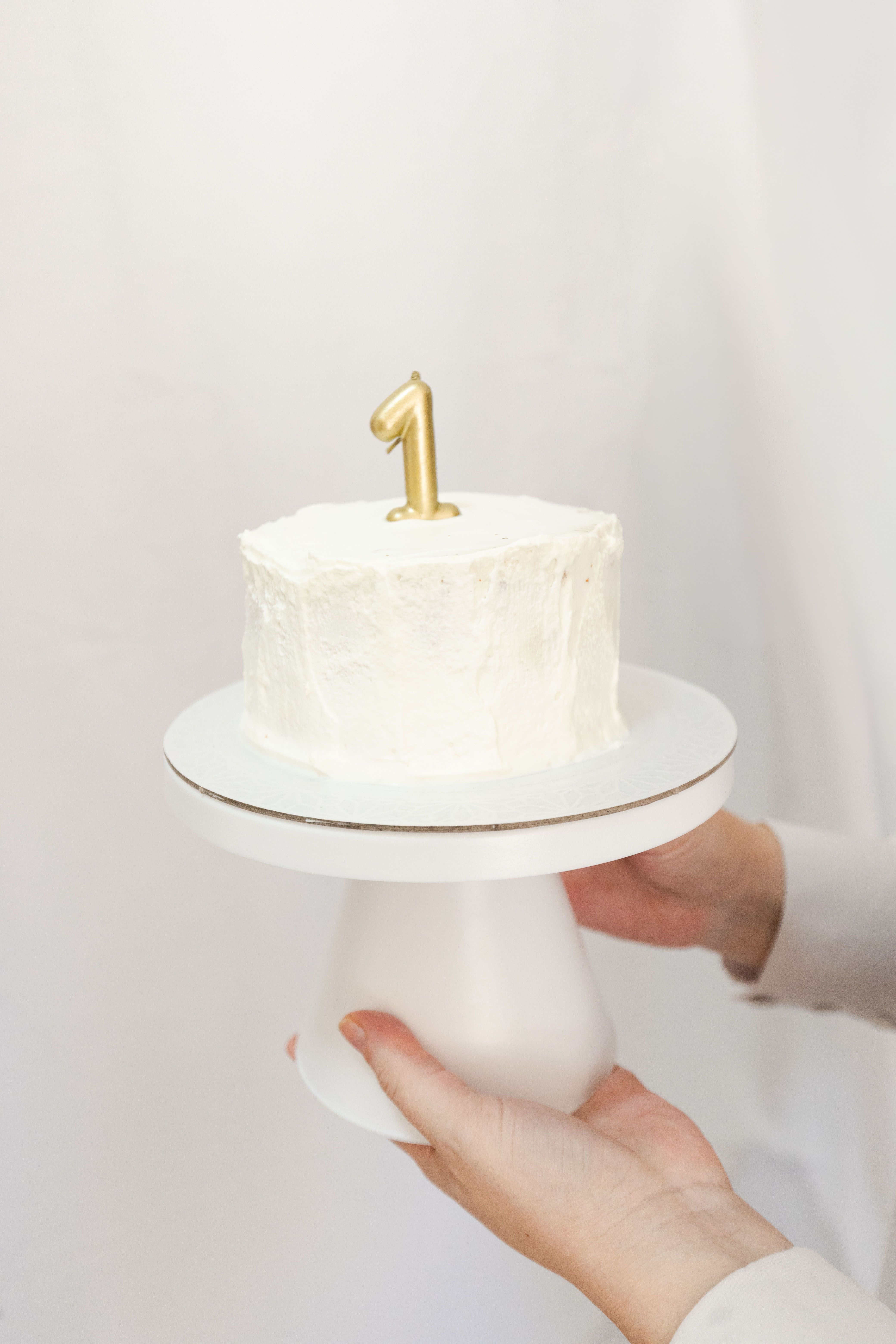 A simple, elegant white cake with a gold number one candle for a first birthday celebration.
