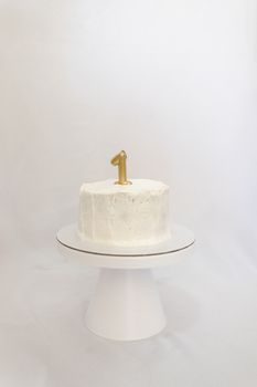 Celebrate a first birthday with this elegant, minimalist white cake featuring a gold number one candle.
