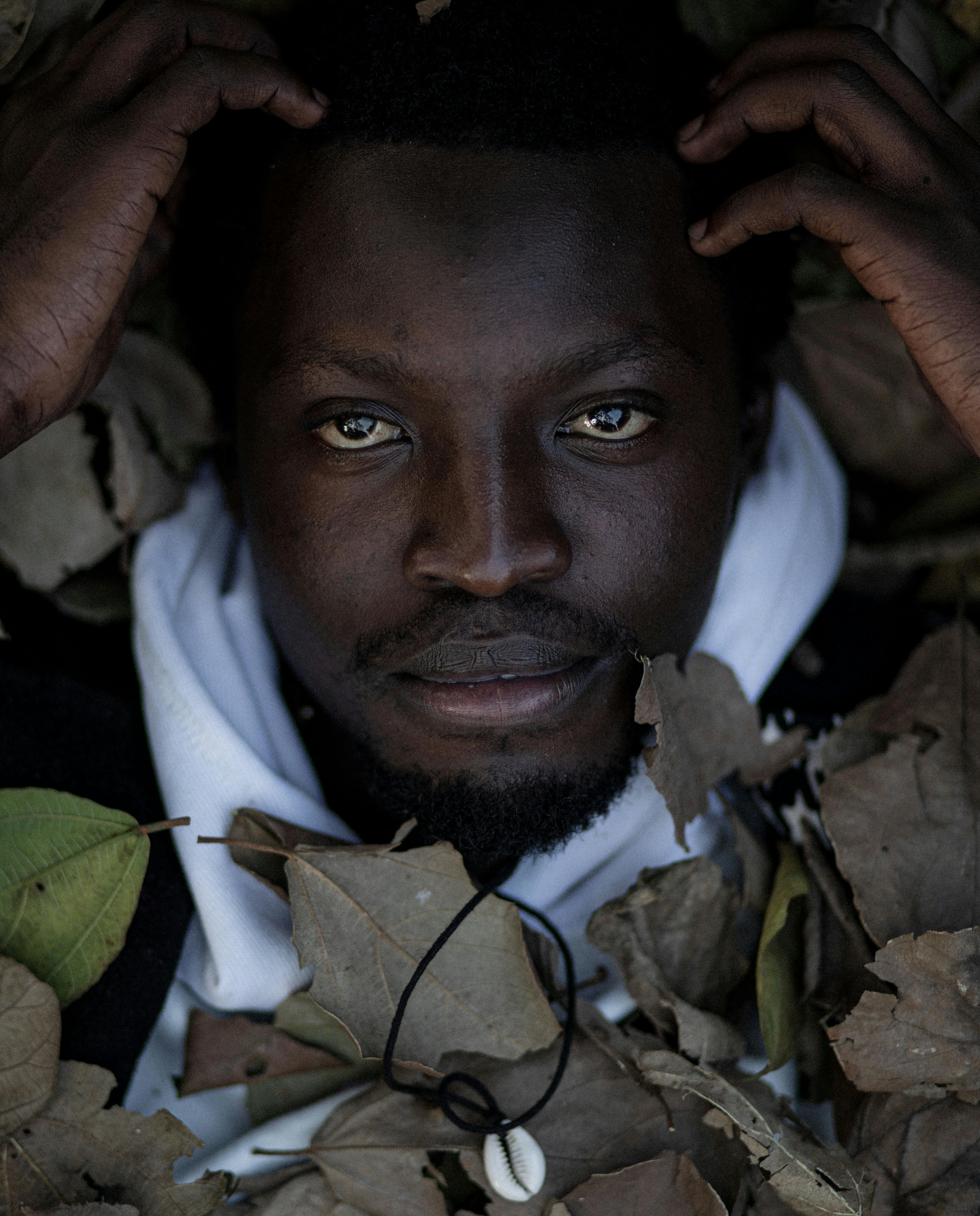 Безкоштовне Крупний план чоловіка, оточеного сухим листям, що створює художню осінню атмосферу. стокове фото