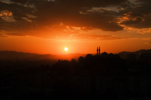 Silhouette of mosque minarets against a vivid orange sunset, creating a dramatic skyline.
