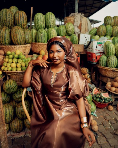 Free A woman in traditional attire poses gracefully amidst a vibrant market of fruits. Stock Photo