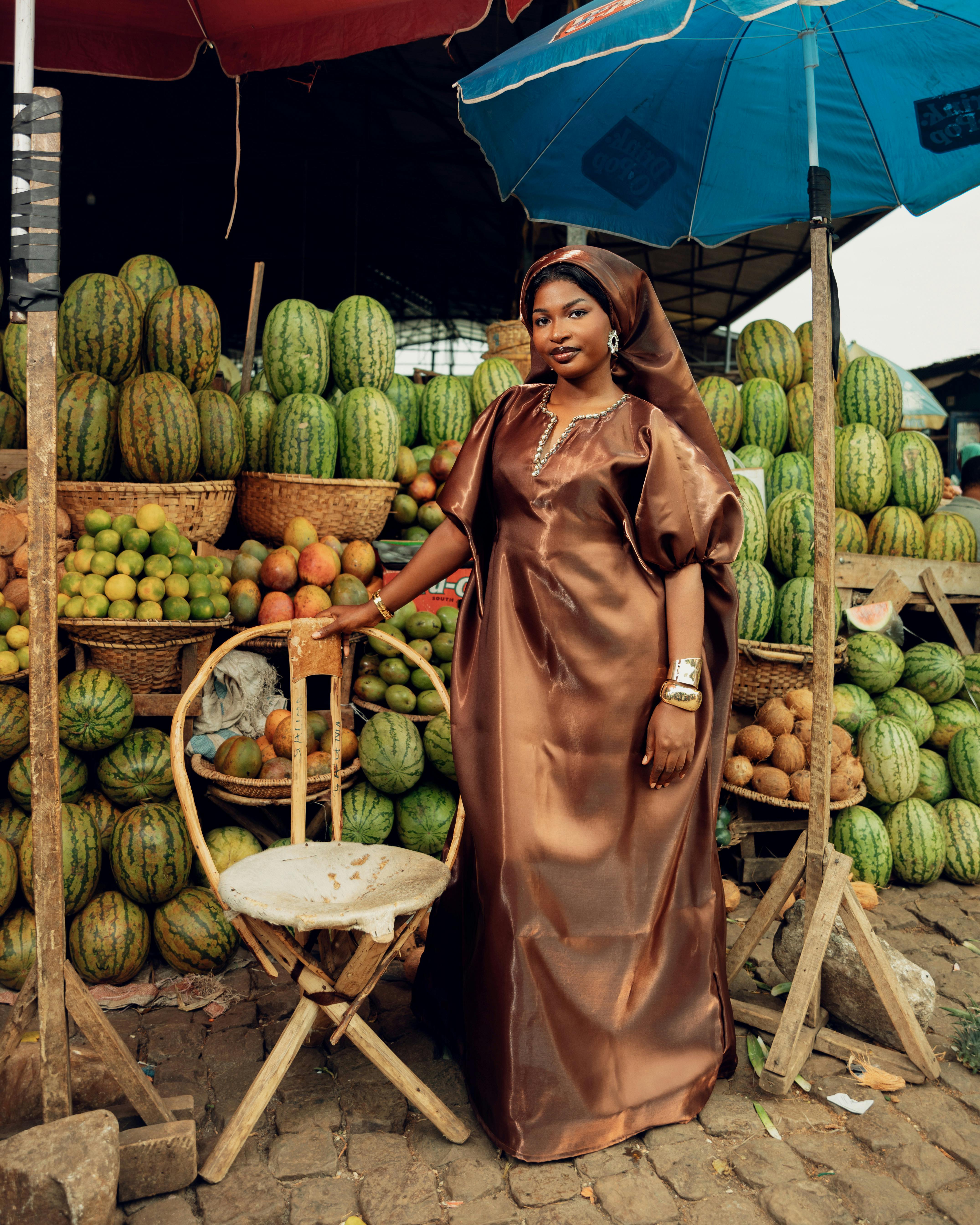 Zadarmo Žena v elegantných hnedých tradičných šatách stojí na farebnom ovocnom trhu s rôznymi melónmi a limetkami. Fotka z fotobanky