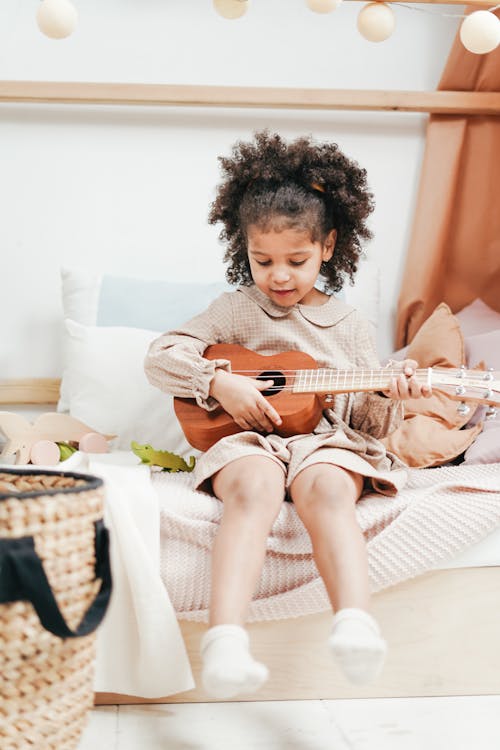 A girl in ackecked long sleeve dress Playing Brown Acoustic Guitar