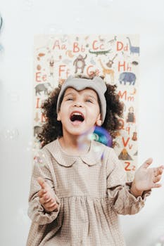 Happy child enjoying bubbles indoors with an educational alphabet poster in the background.