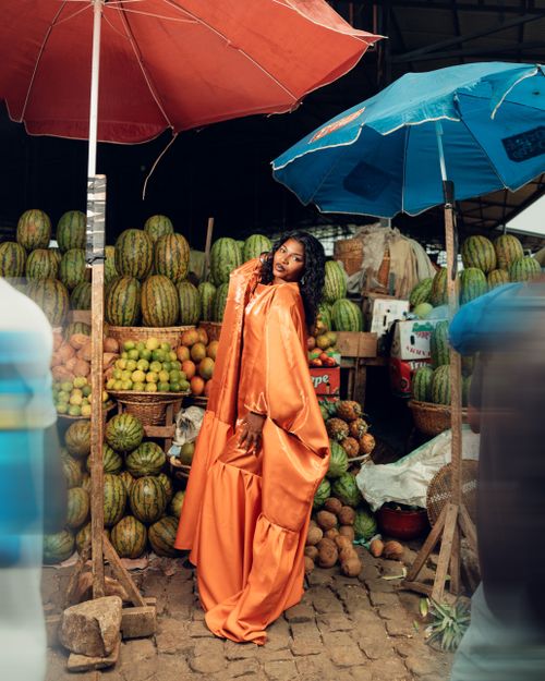 Free Stylish woman in orange dress standing at a bustling fruit market under colorful umbrellas. Stock Photo