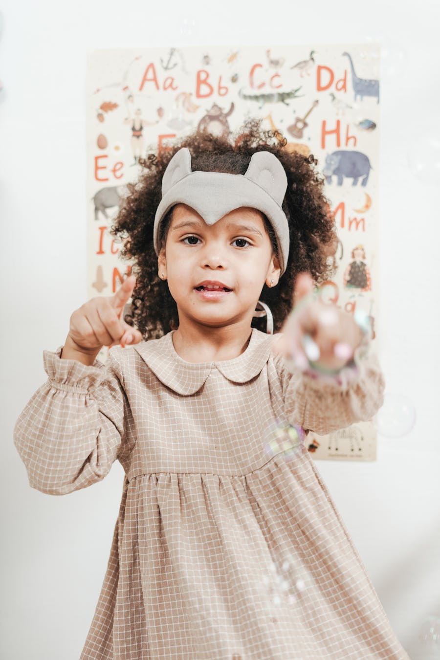 Child in a Peter Pan collar party frock playing with bubbles indoors