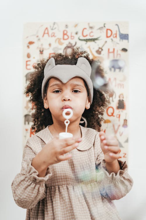 Girl Wearing Brown Dress While Blowing Bubbles