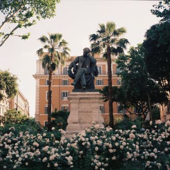 Serene view of a statue in a Roman piazza surrounded by palm trees and flowers.