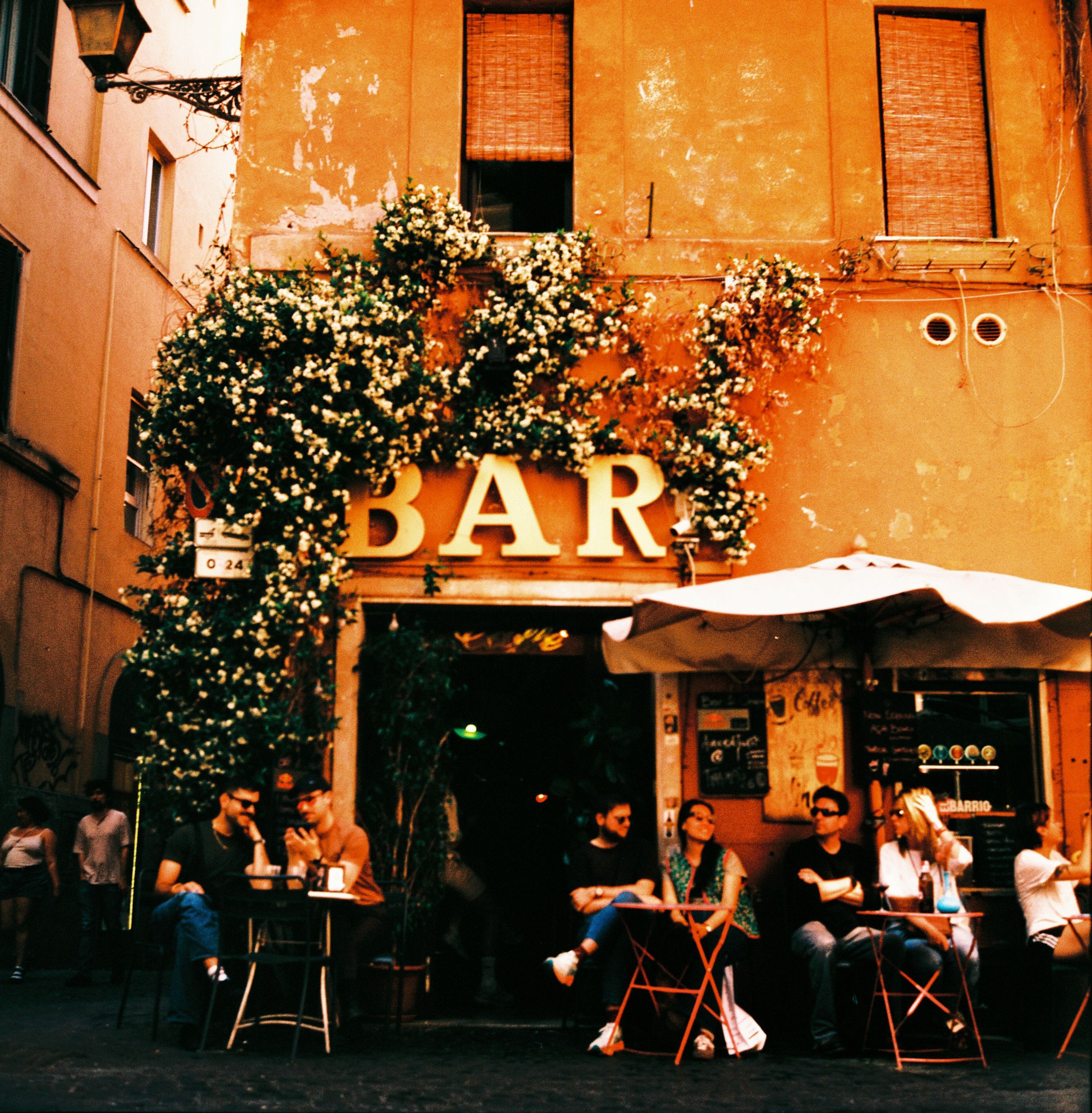 A vintage-style photo of people enjoying a lively cafe scene at a bar in Rome, Italy.