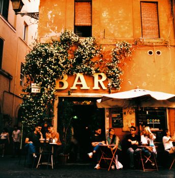 A vintage-style photo of people enjoying a lively cafe scene at a bar in Rome, Italy.