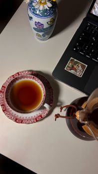 A serene desk scene featuring a cup of tea, laptop, and a floral vase.