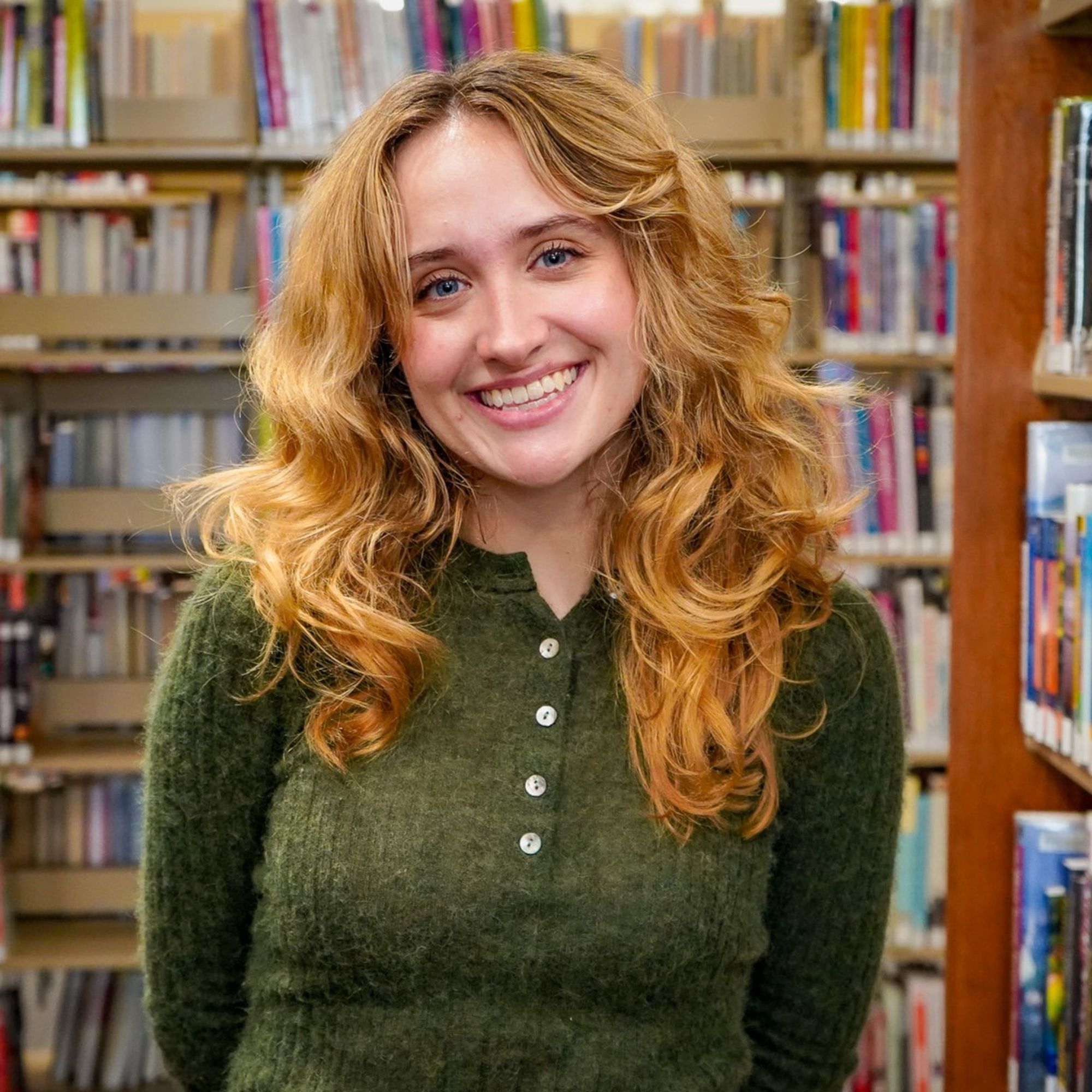 Cheerful young woman smiling while standing in a vibrant library setting.