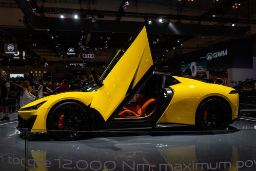 A sleek yellow sports car with butterfly doors showcased at an auto exhibition.
